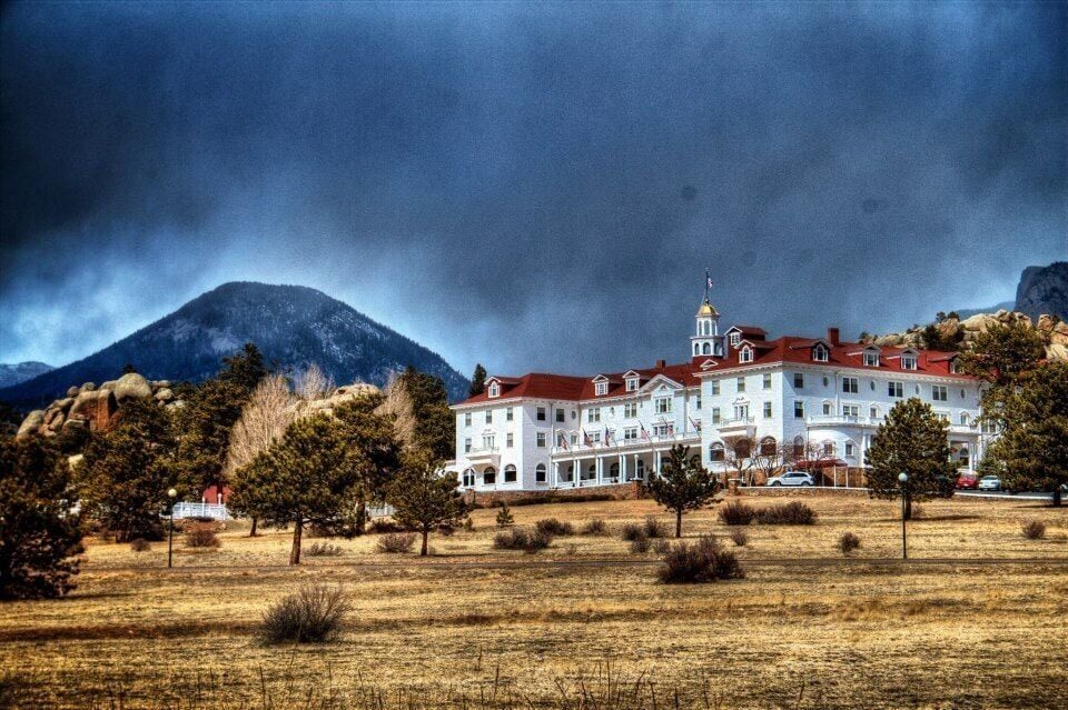 A large white building with a red roof, surrounded by trees and mountains in the background.