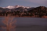 Cordillera montañosa con picos nevados, una masa de agua y una zona boscosa con un pequeño edificio.