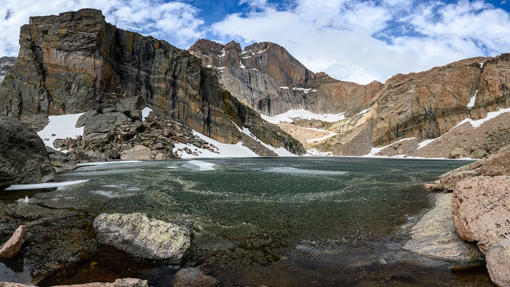 Un paysage montagneux avec un lac glaciaire, entouré de reliefs rocheux et de zones enneigées.