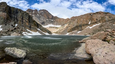 Un paisaje montañoso con un lago glaciar rodeado de terreno rocoso y manchas de nieve.