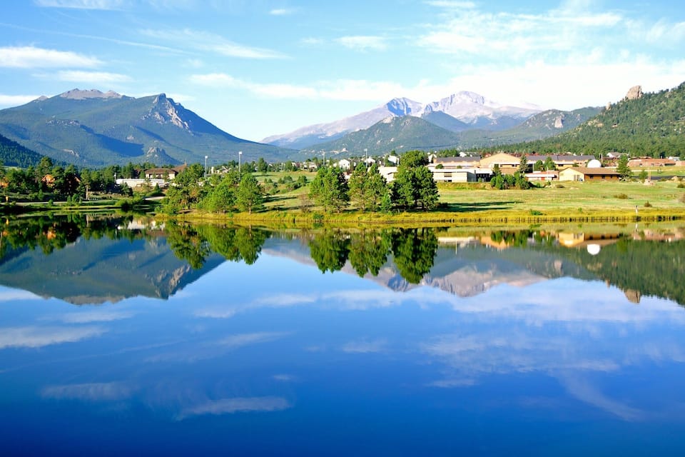 Un lago tranquillo che riflette montagne e un piccolo paese con case e alberi.