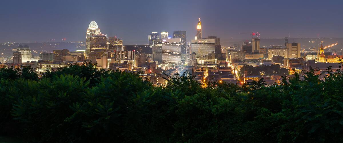 A city skyline at dusk with illuminated buildings and a prominent dome structure.