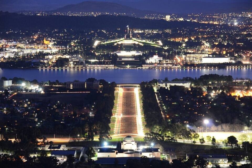 Ein Stadtbild bei Nacht mit einem markanten Stadion, einer großen Wasserfläche und umliegenden Gebäuden.