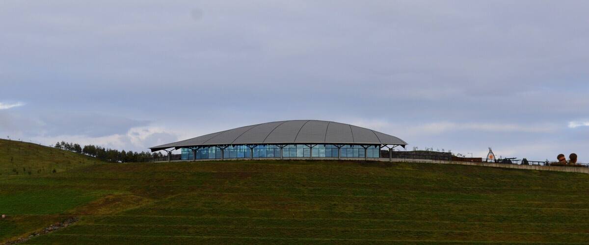 A modern, dome-shaped building on a grassy hill under a cloudy sky.