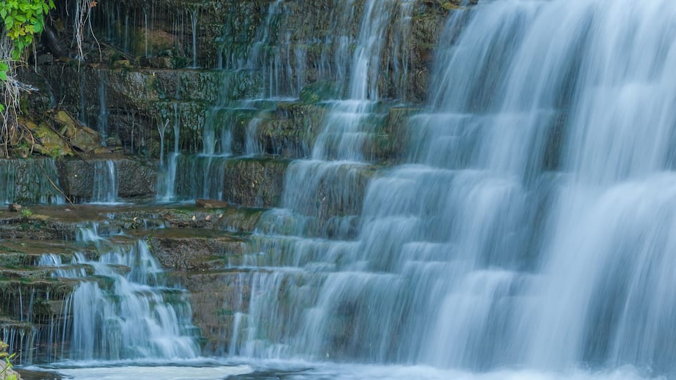 A multi-tiered waterfall cascading over rocks in a forested area.