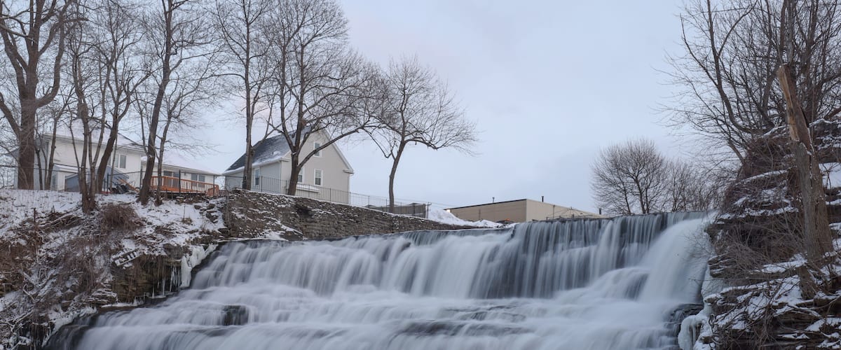 A waterfall cascading over rocky terrain with snow-covered trees and houses in the background.