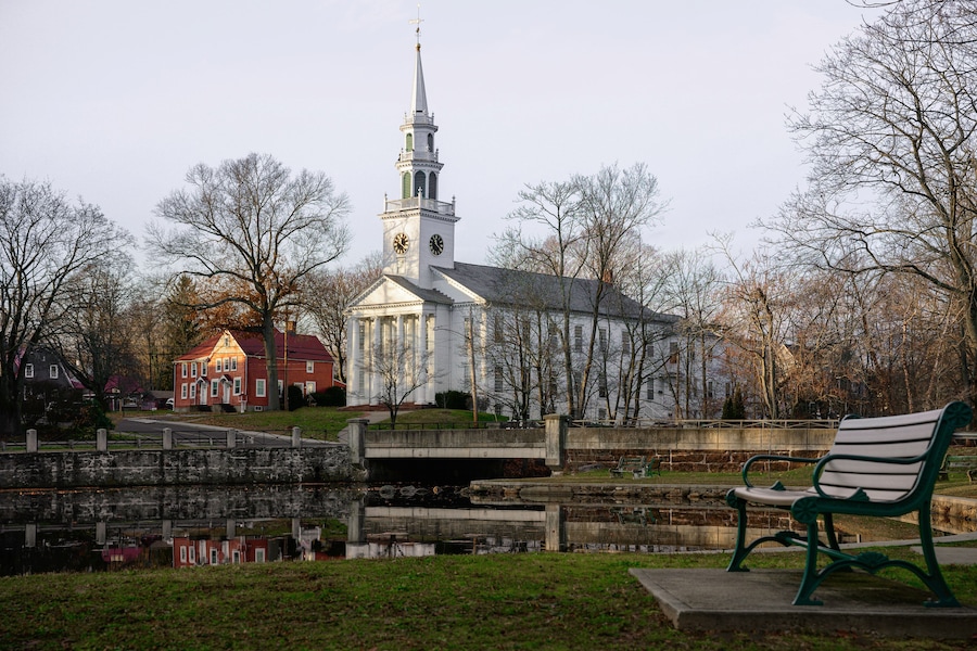 Milford Cityscape in winter over the Wepawaug River with views of the First Church of Christ in Milford built in 1824, stone bridge, and bench at the Lower Lagoon Park green in Connecticut