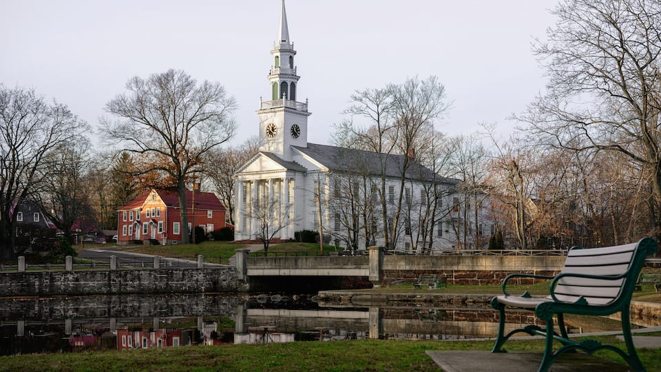 A church with a steeple, a bridge, and a bench in a park.