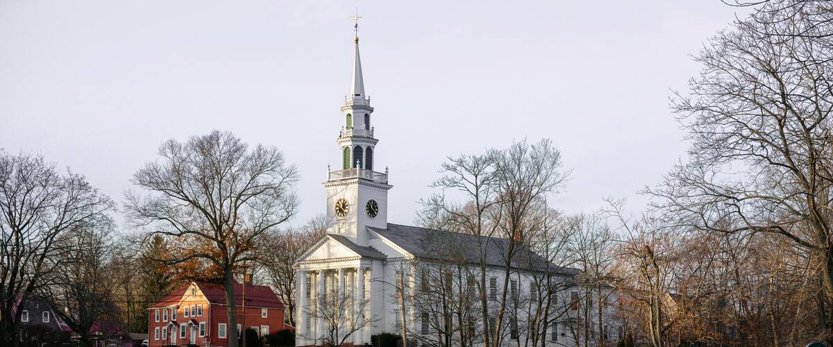 A church with a steeple, a bridge, and a bench in a park.