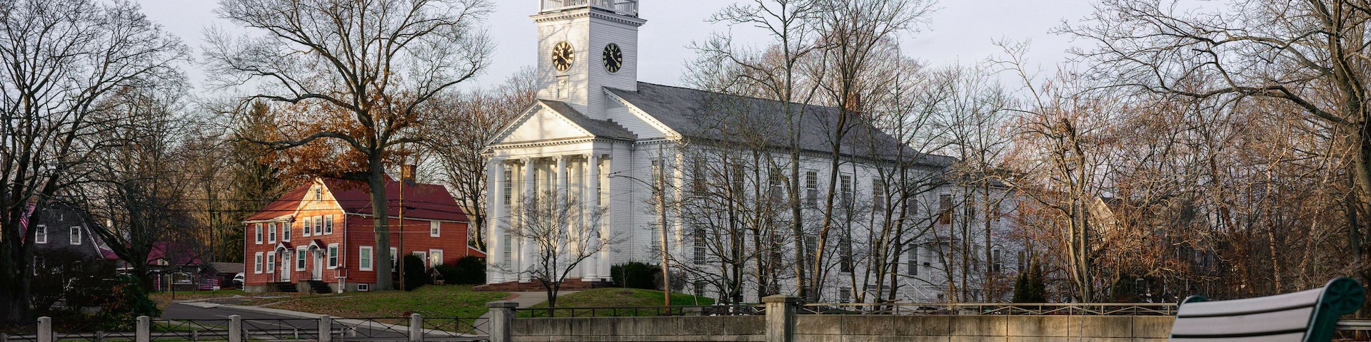 Milford Cityscape in winter over the Wepawaug River with views of the First Church of Christ in Milford built in 1824, stone bridge, and bench at the Lower Lagoon Park green in Connecticut