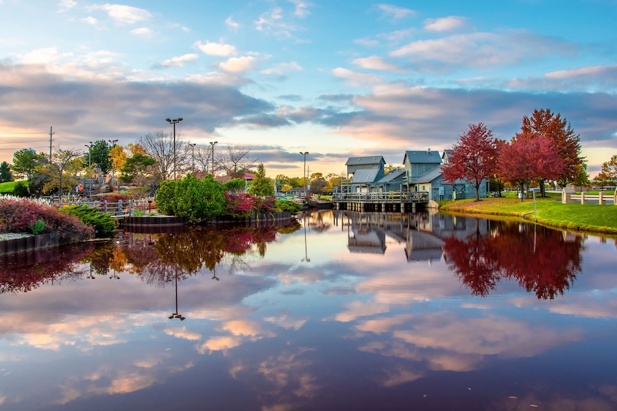 A calm lake reflecting a park with autumn-colored trees, a wooden bridge, and a house.