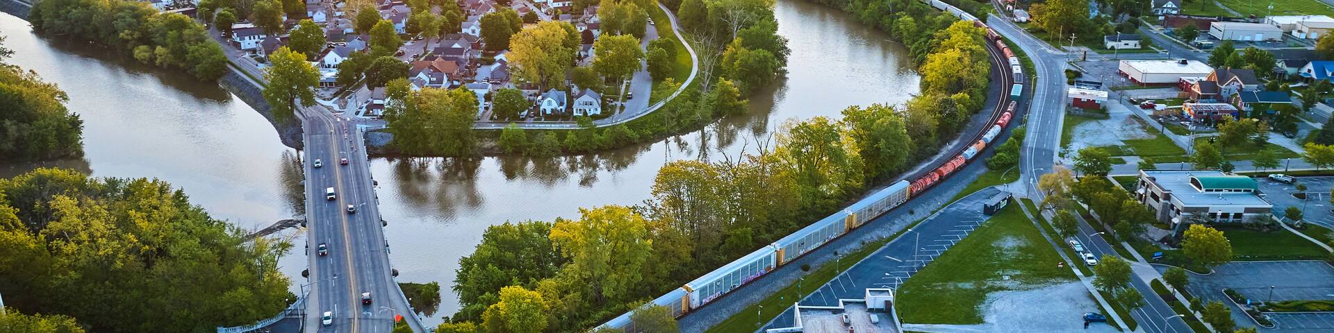 Downtown city and train with bridge over snaking riverbend to neighborhood village aerial cityscape