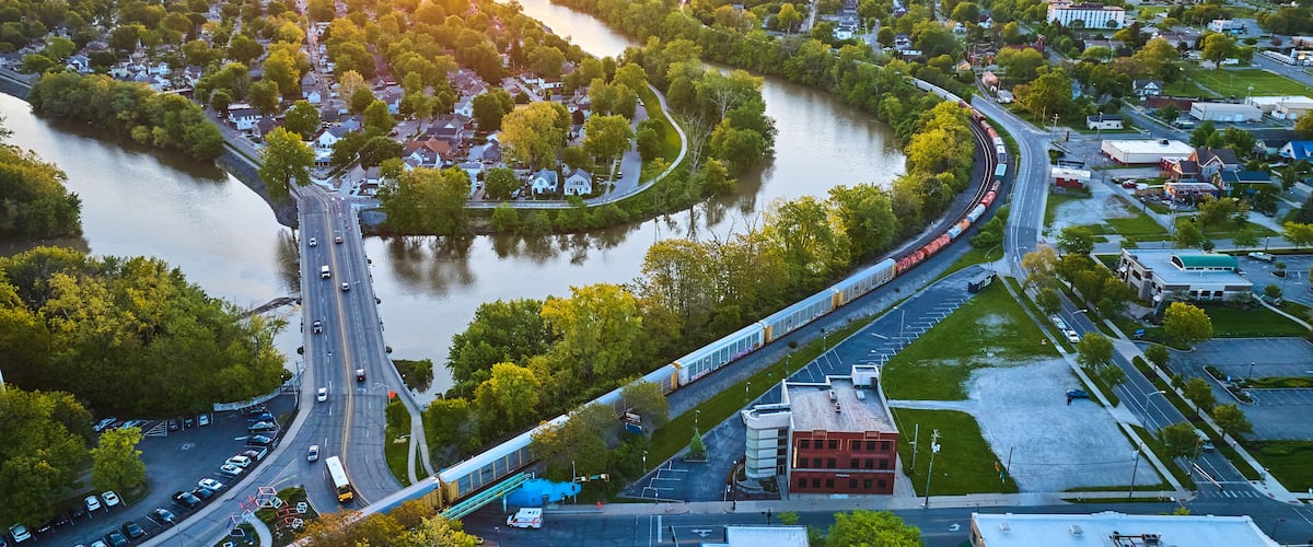 A river winding through a town with a bridge and a train passing over it.
