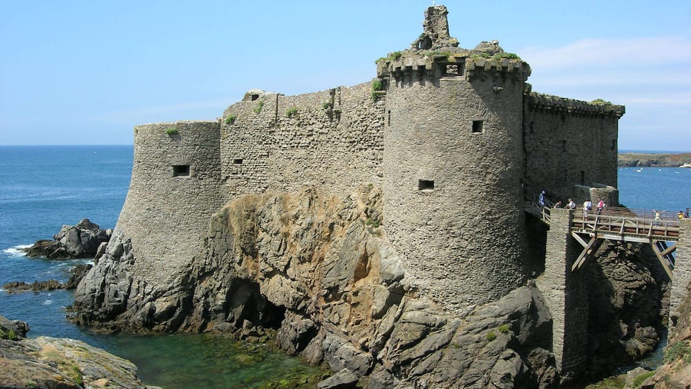 Un château de pierre situé en bord de mer, avec une passerelle en bois.