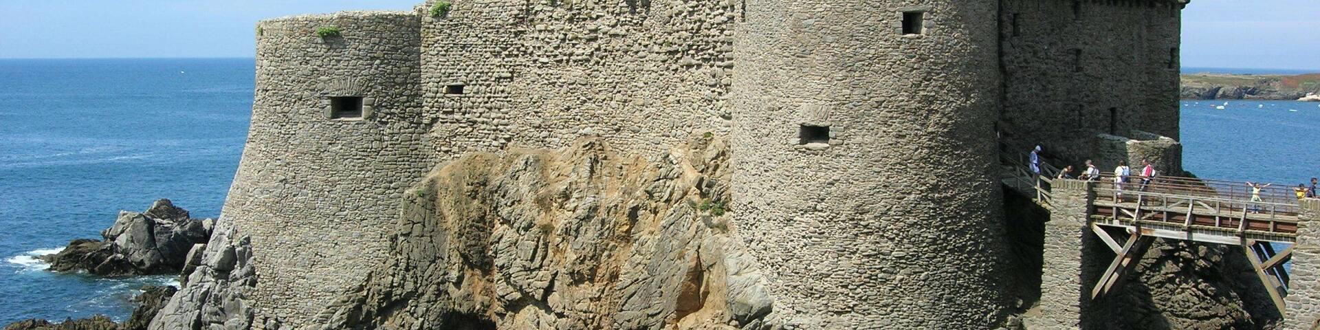 A stone castle by the sea with a wooden walkway.