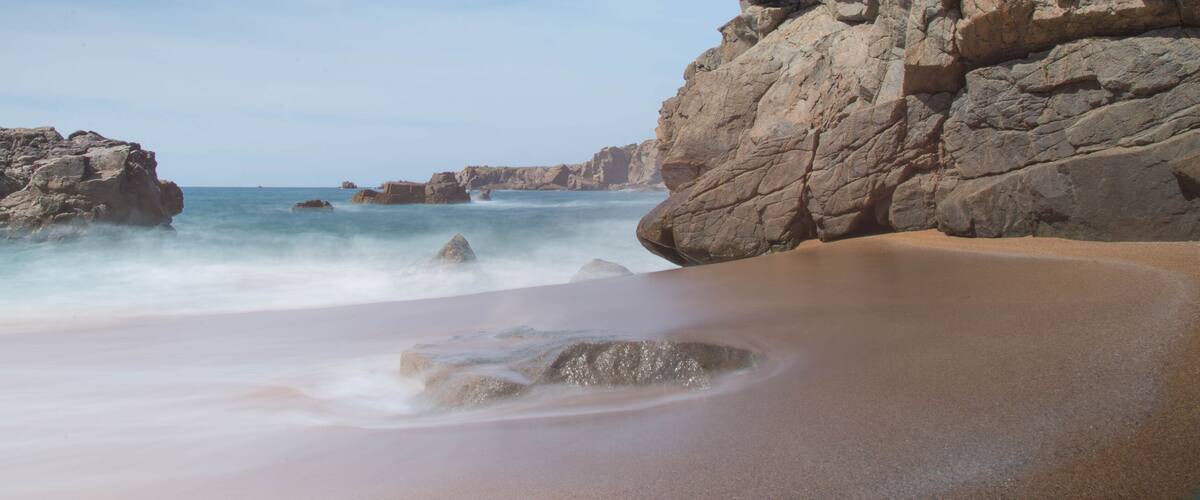 A sandy beach with large rocks and waves crashing onto the shore.