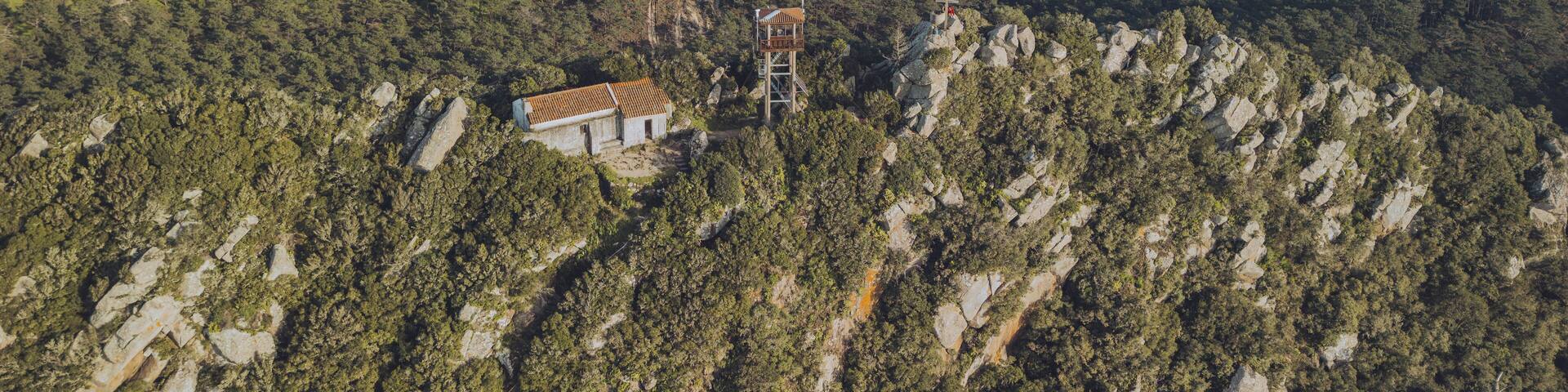 Paisaje montañoso con un edificio pequeño rodeado de bosque denso y terreno rocoso.