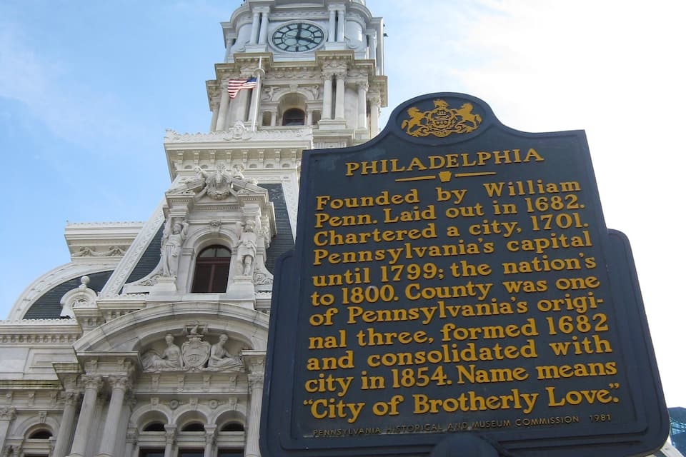 A historical building with a clock tower and a sign detailing Philadelphia's history.
