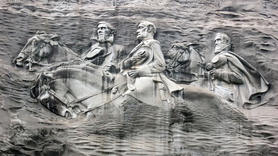 A detailed stone relief of a historical scene with figures on horseback, set against a textured rock background.