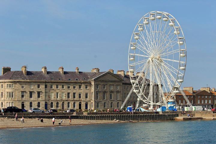 A large Ferris wheel, a waterfront promenade, and historic buildings along the shore.