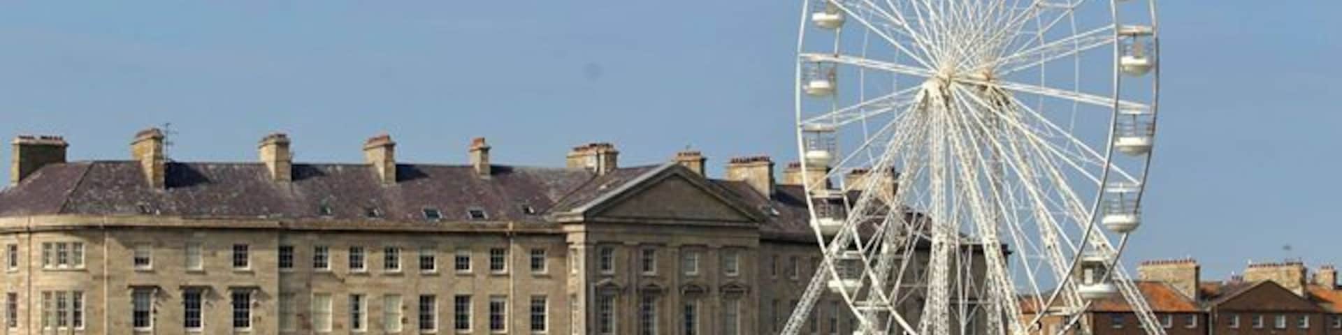 A large Ferris wheel, a waterfront promenade, and historic buildings along the shore.