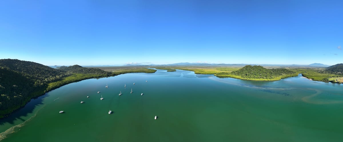A large body of water with several boats, surrounded by green hills and distant mountains under a clear blue sky.
