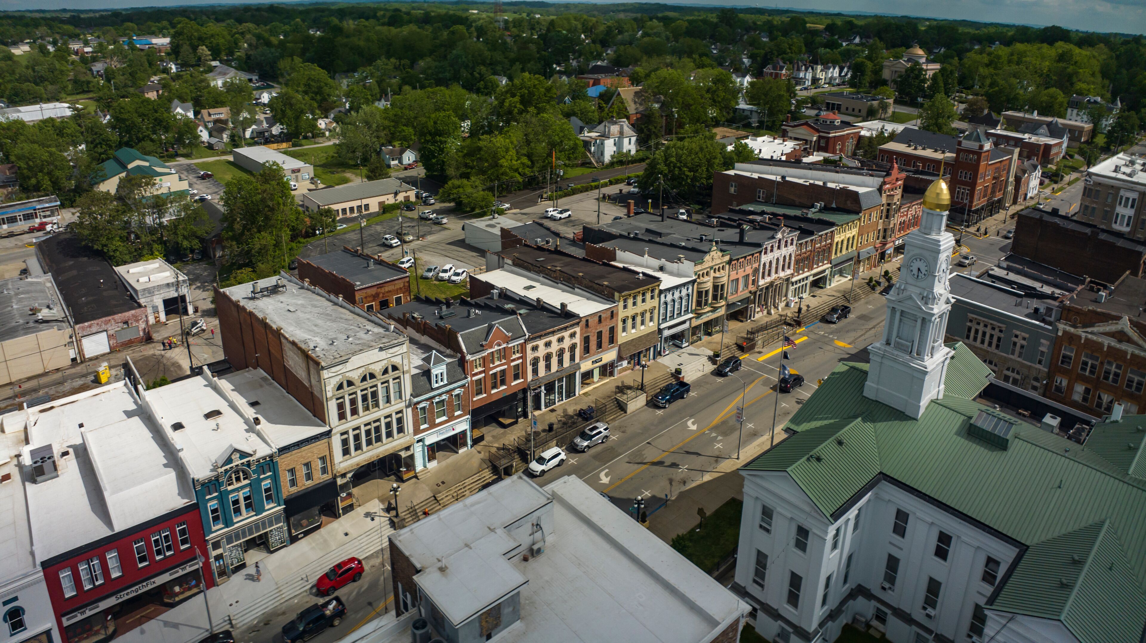 An aerial view of a historic town with a prominent clock tower, narrow streets lined with historic buildings, and a mix of commercial and residential areas.
