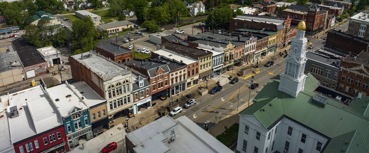 An aerial view of a historic town with a prominent clock tower, narrow streets lined with historic buildings, and a mix of commercial and residential areas.
