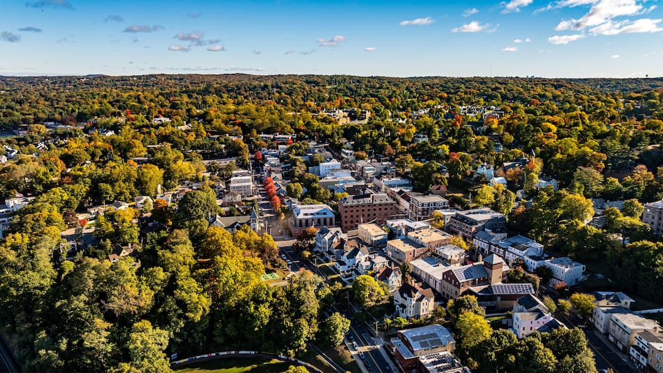 An aerial view of a town surrounded by dense forests with autumn foliage.