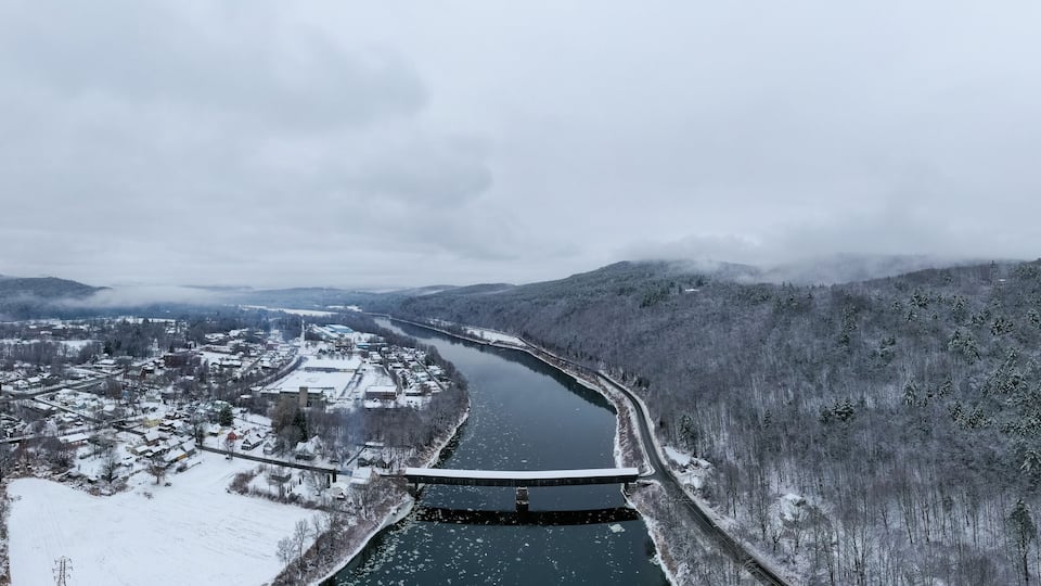 A snow-covered river valley with a bridge and a town.