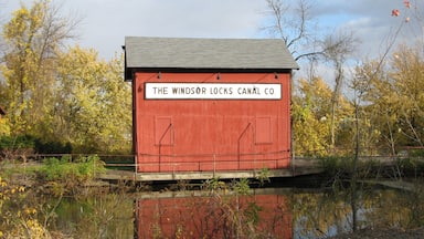 Um edifício vermelho com uma placa que diz 'The Windsor Locks Canal Co.', rodeado de árvores e um corpo de água.