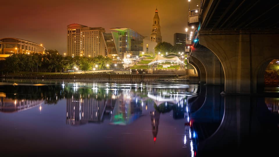 Hartford downtown night cityscape and Founder's bridge reflected on Connecticut River. Brilliant city lights illuminating the dark sky and purple river water.