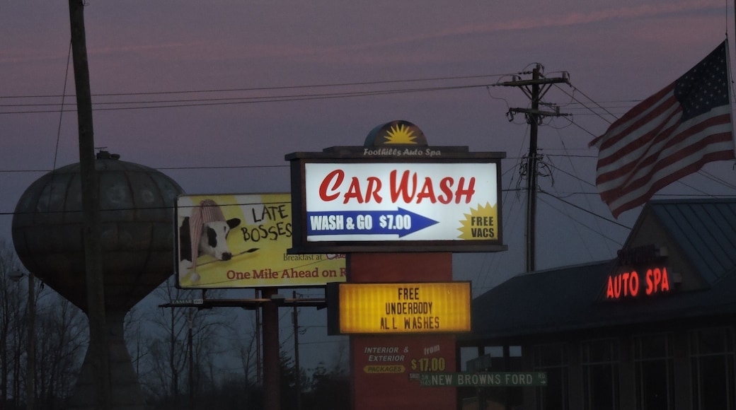 #AppalachianEchoes
"Here we have a proud American country-town." I like the staggering towers: the carwash sign followed by the billboard, then water-tower. The illumination of the car sign makes locality and closeness appear important to this town, yet that does not signify complete isolation from consumerism, due to the Chick-fil-A billboard, a relatable fast-food chain to the south. They almost contradict one another, until the viewer realizes they can work together, especially under the other tower- distanced to the far-right, the American Flag. Yet, as if the America flag isn't enough alone, paired with my favorite part, the small sign reading, "DON'T SETTLE FOR LESS," this image simultaneously becomes a perfect capture of the American Dream in the heart of the south.