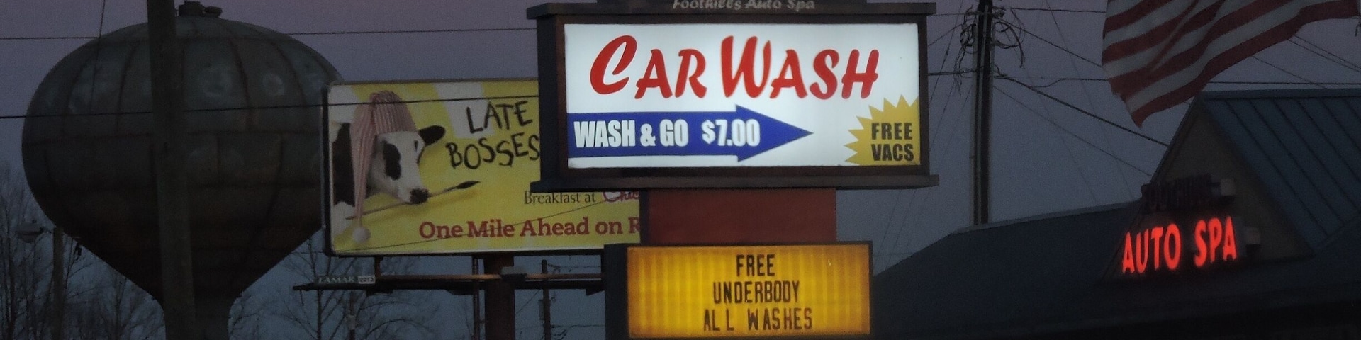 #AppalachianEchoes
"Here we have a proud American country-town." I like the staggering towers: the carwash sign followed by the billboard, then water-tower. The illumination of the car sign makes locality and closeness appear important to this town, yet that does not signify complete isolation from consumerism, due to the Chick-fil-A billboard, a relatable fast-food chain to the south. They almost contradict one another, until the viewer realizes they can work together, especially under the other tower- distanced to the far-right, the American Flag. Yet, as if the America flag isn't enough alone, paired with my favorite part, the small sign reading, "DON'T SETTLE FOR LESS," this image simultaneously becomes a perfect capture of the American Dream in the heart of the south.