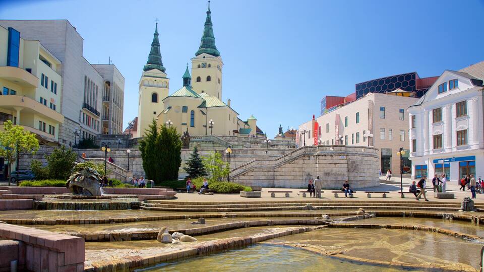 A historic square with terraced pools, a church with twin spires, and surrounding modern buildings.