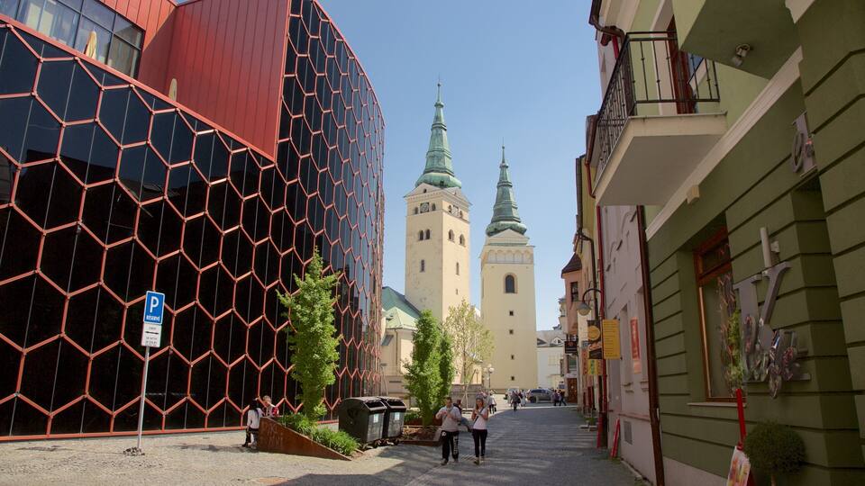 A street with modern buildings, a church with two towers, and pedestrians.