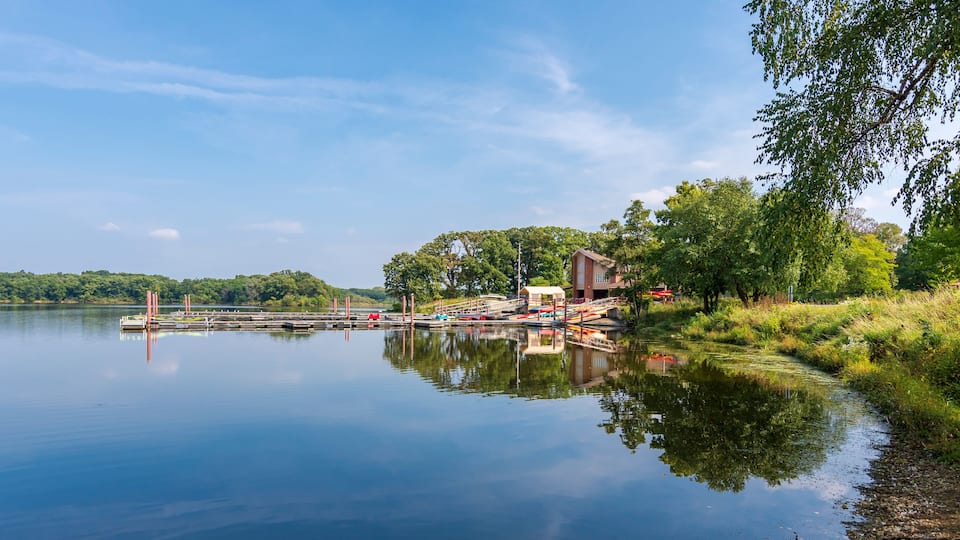 A calm lake with a dock, a small building, and lush greenery.