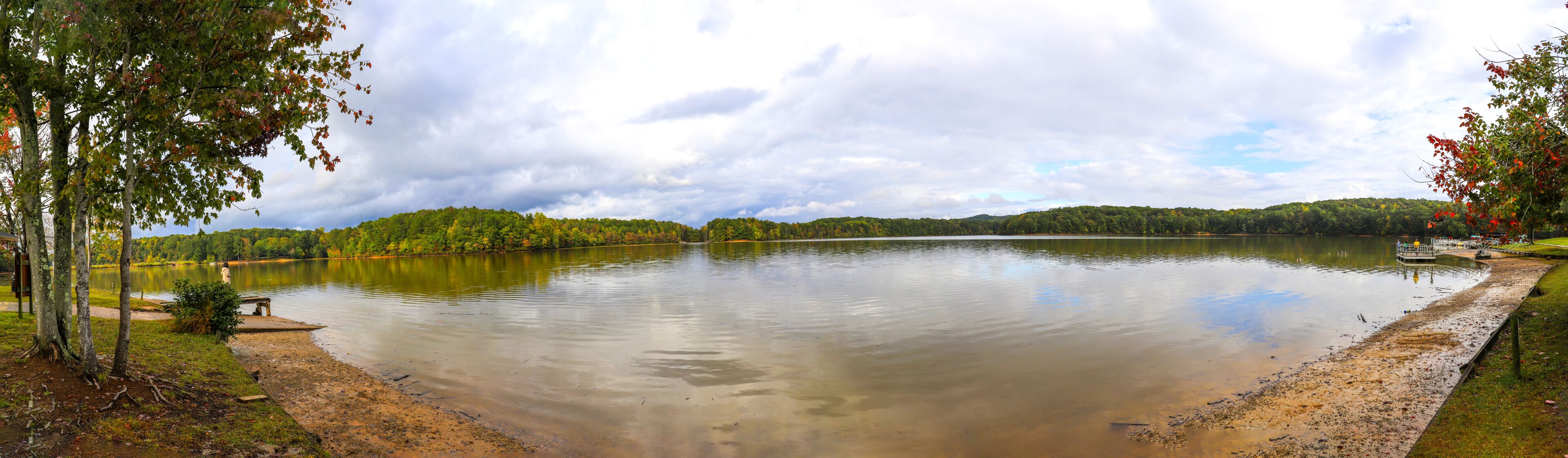 a breathtaking panoramic shot of the vast still lake water and lush green and autumn colored trees with powerful cloud covers at Sweetwater Creek State Park in Lithia Springs Georgia