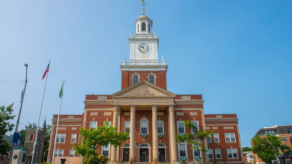 A red-brick building with a clock tower, columns, and a flagpole.