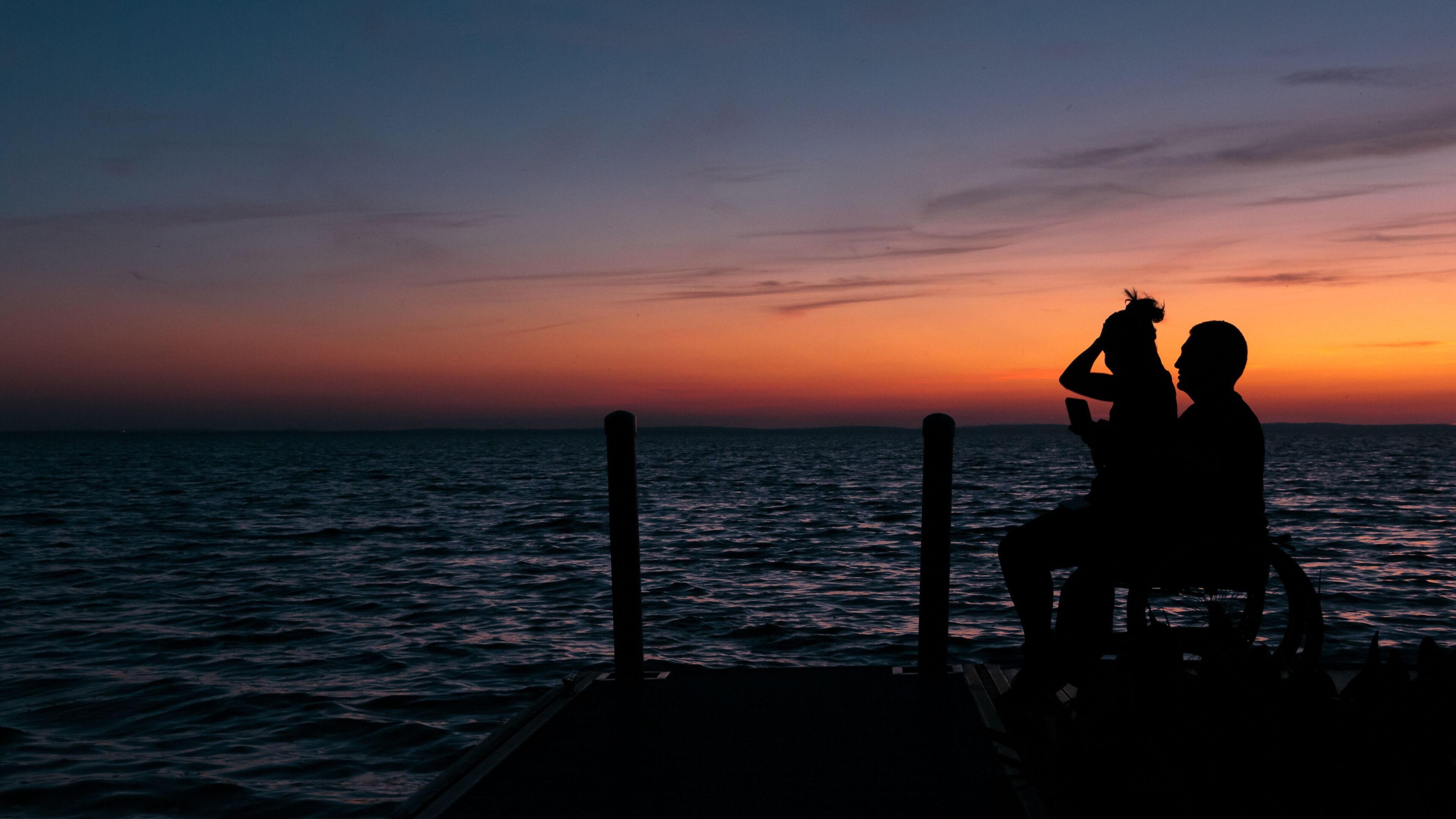 Silhouette of a disabled young man and his girlfriend in a wheelchair enjoying the sunset over Lake Apopka near Orlando, Florida.