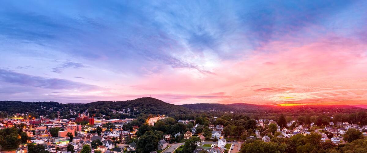 A town at sunset with a colorful sky, rolling hills, and a mix of residential and commercial buildings.