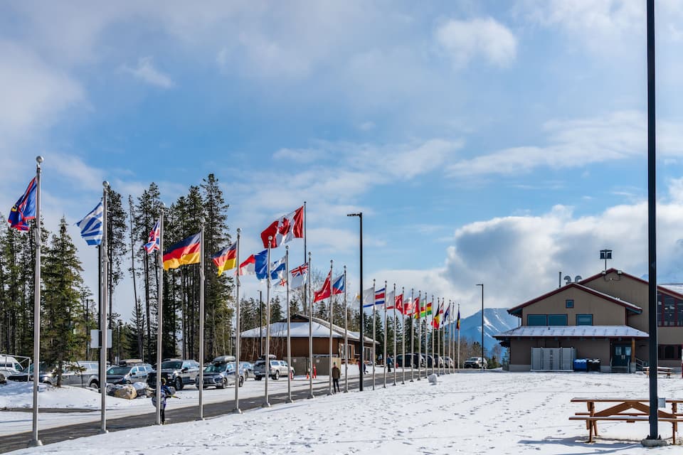 A snowy parking lot with multiple flags, a building, and a mountain in the background.
