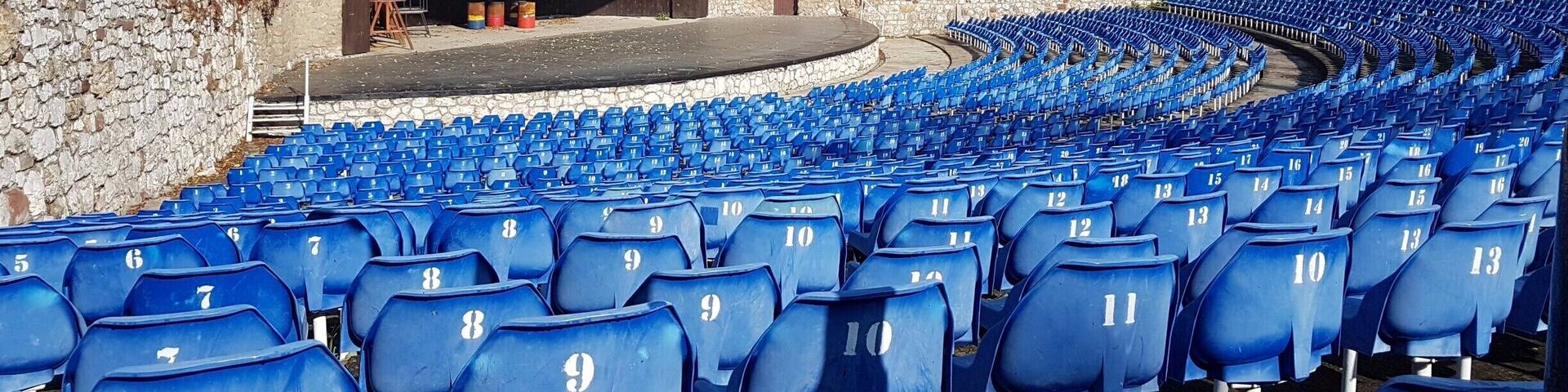 An outdoor amphitheater with blue seats and stone walls.