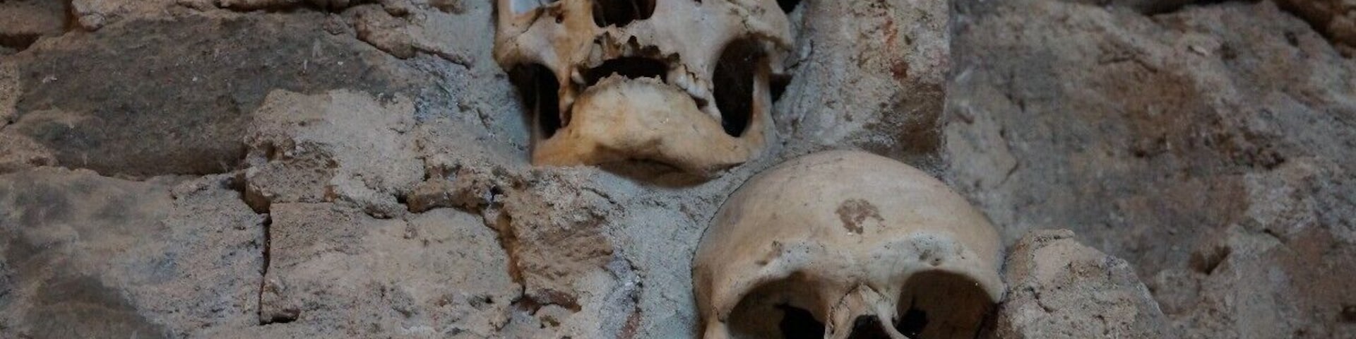 Duas caveiras humanas incrustadas numa parede rochosa.