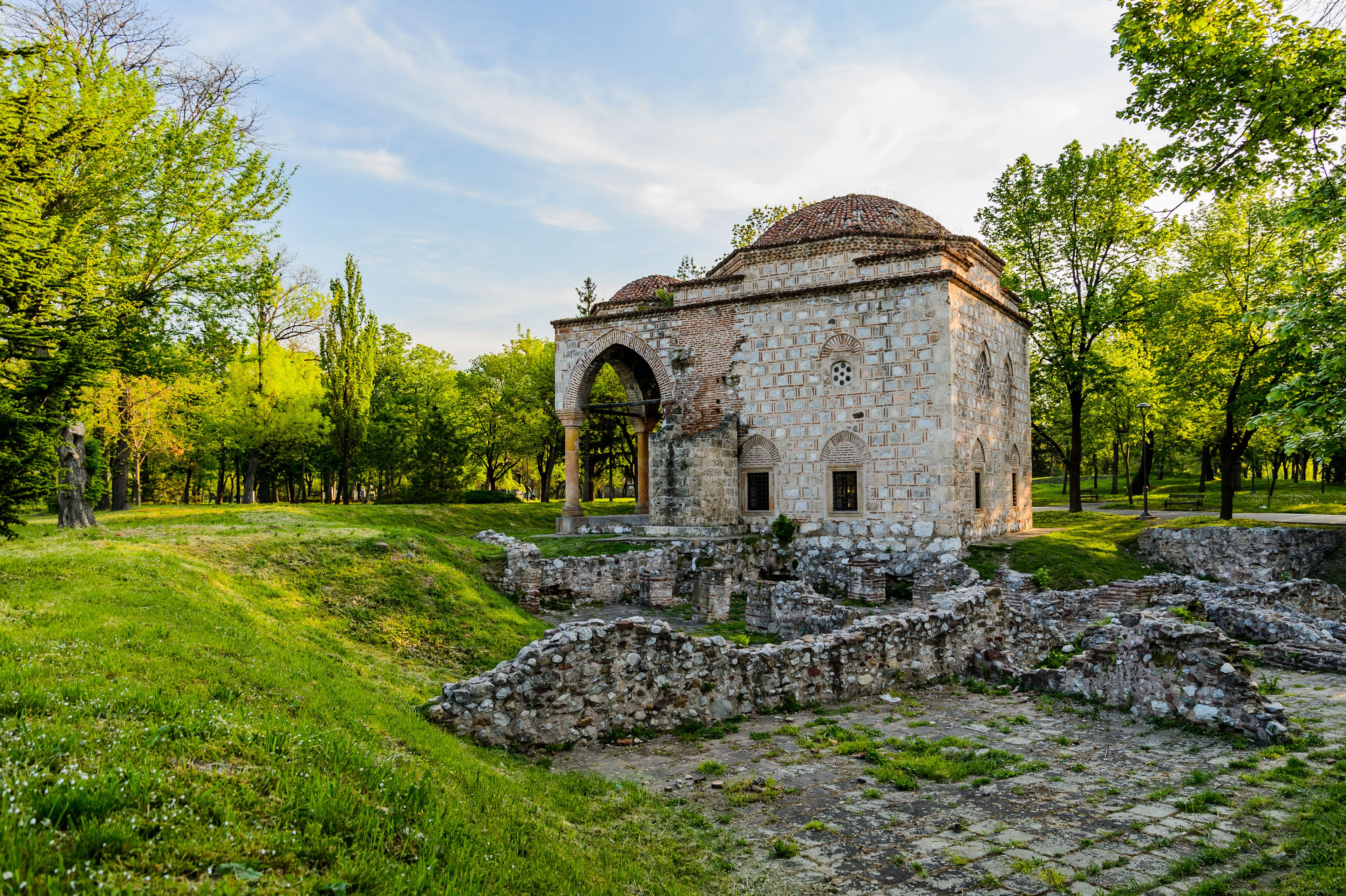 An ancient stone structure with a dome roof, surrounded by lush greenery and trees.