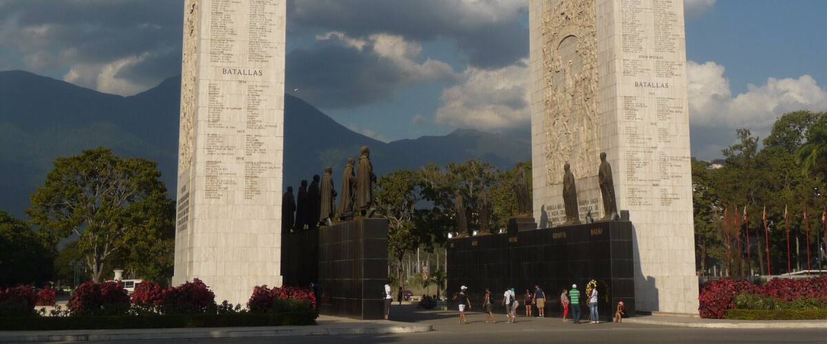 Two large stone monuments with inscriptions, surrounded by trees and mountains in the background.