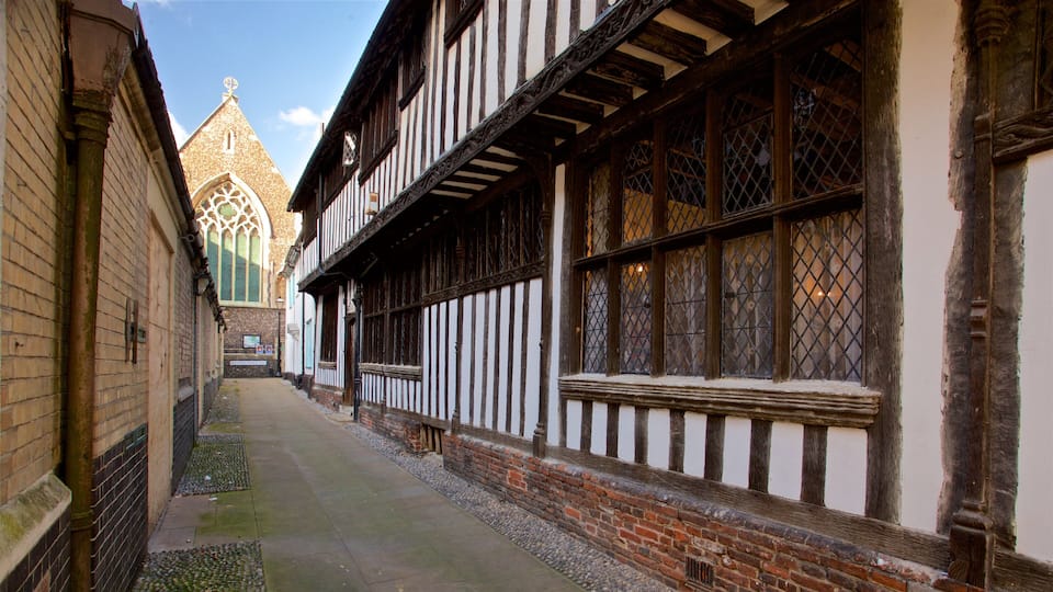A narrow medieval street flanked by timber-framed half-timbered buildings with a church steeple in the background.