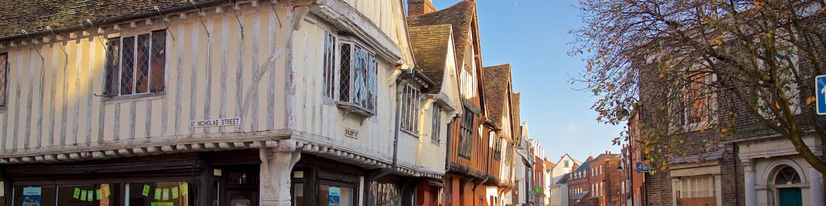 A street lined with historic timber-framed buildings, a red car parked on the side, and a clear blue sky.