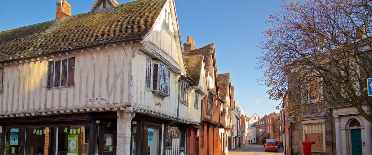 Une rue bordée de bâtiments historiques à colombages, une voiture rouge garée sur le bord et un ciel bleu azur.