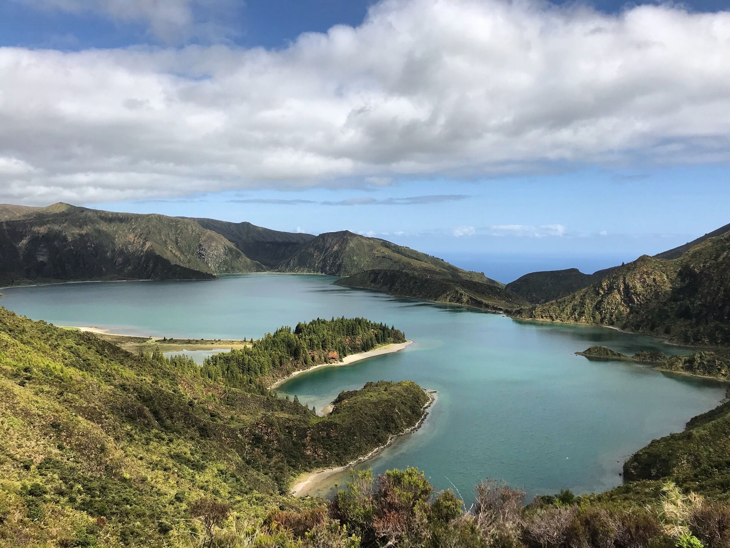 Paisagem montanhosa com um lago grande, rodeado por florestas densas e colinas.